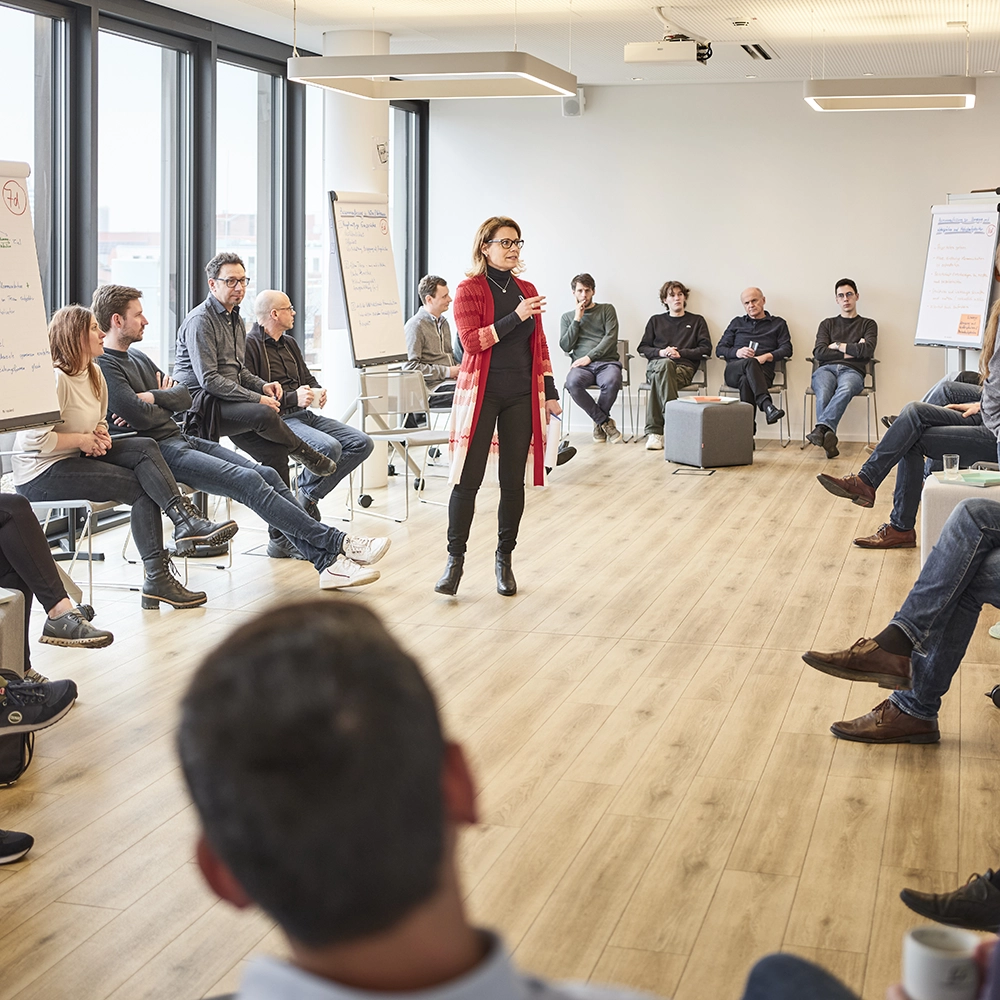 Das Bild zeigt eine Gruppe von Menschen in einem Kreis sitzend und eine Person in der Mitte.